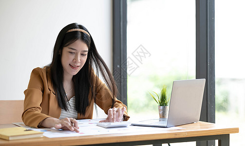 亚洲女商务人士在办公室用笔记本电脑在线支付账单的画像 有计算机和支票簿的漂亮女孩 快乐地支付账单 启动业务财务计算帐户概念金融桌图片