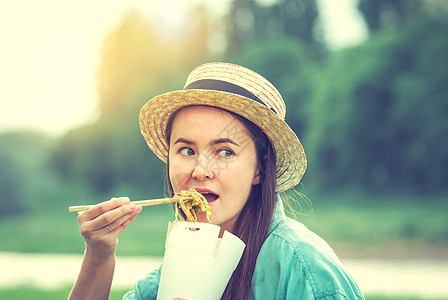 青春的caucasian年轻女人 在日落时吃泰语食物筷子午餐盘子帽子朋友们美食女性异国面条街道图片