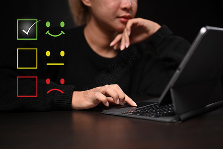 年轻女性使用计算机平板来选择微笑脸图标 以评价产品和服务的产品和服务图片