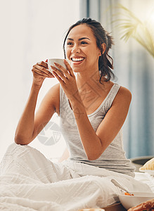 一位美丽的年轻西班牙裔女性早餐享用一杯热咖啡 一位混血女性坐在床上笑着喝茶图片