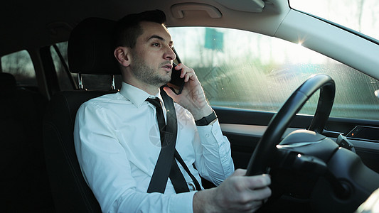 英俊的年轻男子司机骑车和打电话 使用智能手机交谈 边开车边说话 生活方式 道路 汽车概念图片