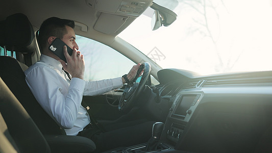 商务人士在商务舱汽车旅行时正在用他的智能手机交谈 成功的生活方式 年轻的商务人士在车里用手机聊天图片