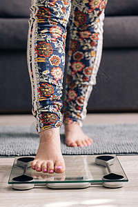 女孩的腿踩在体重计上 标度的少妇测量重量 人体赤脚测量体脂超重 检查 BMI 减肥的苗条女人 饮食女性脚站在房间里的体重秤上图片