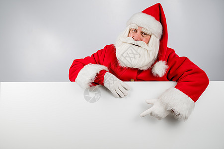 圣诞老人从白色背景中探出头来 用手指指着一个空旷的地方 圣诞节快乐假期祖父男性问候语胡须庆典帽子木板戏服卡片图片