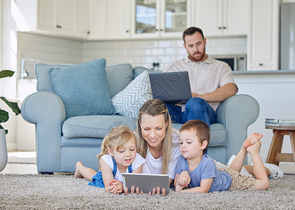 母亲和两个孩子在数字平板电脑上看东西 小女孩和男孩观看教育卡通视频或使用平板电脑进行视频通话 爸爸在家工作图片