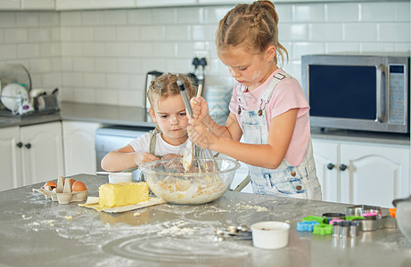 两个凌乱的小女孩在家里的厨房里烘烤 专注于白种人的姐妹们正在学习制作甜点和做饭 可爱的孩子们互相帮助 为房子准备食谱图片