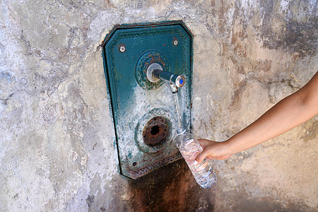 妇女用手从墙上的喷泉中填充塑料瓶水 即饥渴和水危机概念图片