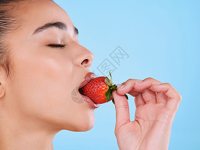 演播室拍到一个有魅力的年轻女人 在蓝色背景下咬草莓 她非常喜欢健康图片