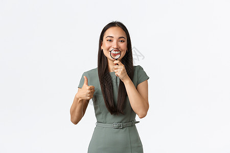保健 美容和口腔学概念 满足了具有吸引力的像亚洲女性在牙医办公室白牙 用放大玻璃对嘴唇表示完美的微笑 并在批准时举起拇指电子商务图片