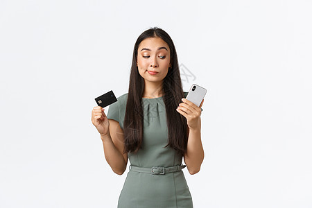 绿色裙子小仙子小企业主 女企业家的概念 犹豫不决 持怀疑态度的亚洲女性尝试新的银行应用程序 并在出示信用卡时对智能手机屏幕持怀疑态度裙子经理房背景