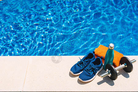 游泳池前的运动配件 橙色毛巾 蓝色水瓶 重量 花园游泳池的背景图片