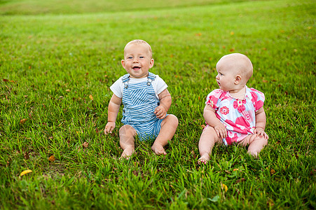 两个快乐的男婴和一个9个月大的女婴 坐在草地上交流 聊天 互相看对方图片