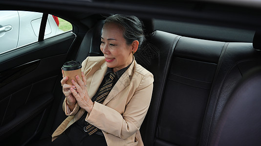 坐在汽车后座客座和喝热咖啡的中年女性创业者微笑着笑图片