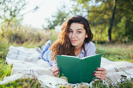 美丽的年轻女学生会读书 读书 躺在自然中的草地上教育休闲成人摄影学生眼镜服装微笑音乐享受图片