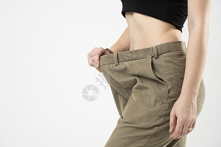 穿着米色长裤的妇女的侧面观点 显示白种背景体重下降的结果 饮食概念和体重减退图片