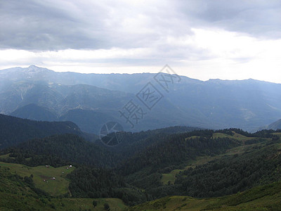 一片全景的山地景观 其山谷和森林山峰在高覆云天下蓝色石头木头山脉爬坡道假期场景冒险房子地平线图片