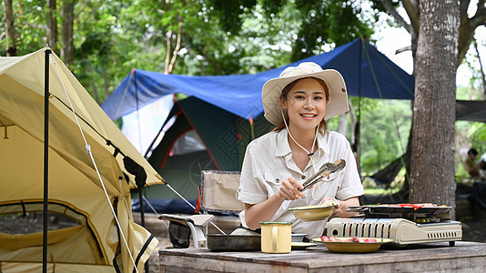 住在露营帐篷附近的年轻女游客 在便携式煤气炉上为晚餐做饭准备餐饮和旅行 探险和度假概念图片