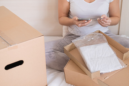 一名无脸妇女坐在床上 开着订货 持有智能手机和信用卡 (请查看InfoFinland上的官方网站)图片