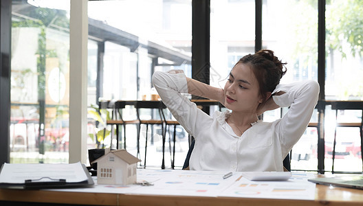 身着衬衫的快乐年轻女性的画像 她坐在办公室的工作场所休息 懒惰的女人伸着手图片