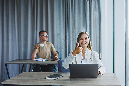 戴眼镜的迷人年轻女性坐在一张桌子旁 在联合办公空间里拿着笔记本电脑 并与同事讨论项目计划 办公室的工作流程团队女士商业营销互联网图片