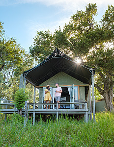 在南非 亚裔女性和欧裔男性在旅行期间在一个帐篷营地小屋里露营假期冒险椅子乡村荒野夫妻小木屋游客大草原衬套图片