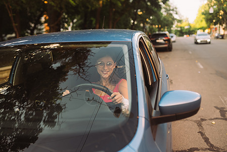 美丽的微笑的女子驾驶汽车 女孩坐在汽车里窗户喜悦运输司机租赁车轮商务商业考试车辆图片