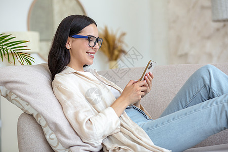 一位戴眼镜的年轻漂亮黑发女性坐在沙发上 用电话开心地笑着阅读检查细胞技术微笑视频客户购物休闲装社会图片
