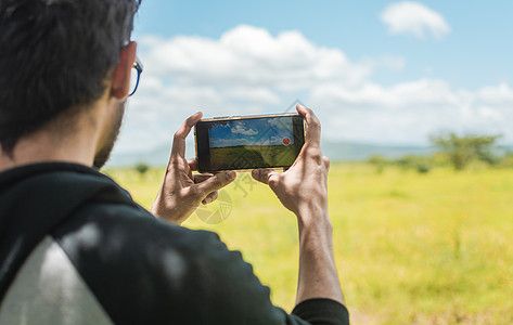 一个人用手机在田野里拍照的后视图 一个男人在田野里拍照的后视图 游客特写镜头在风景中拍照图片