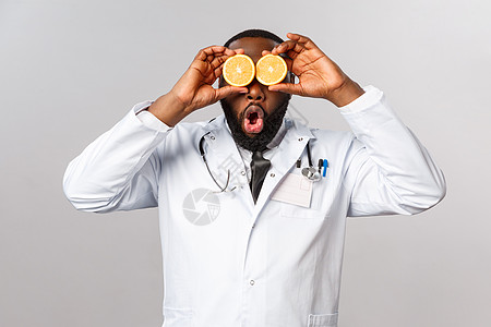 医疗保健 健康饮食和疾病概念 有趣的帅气医生 玩橙子的非裔美国医生 看起来很有趣 告诉大家注意安全 吃维生素和水果 灰色背景医师图片