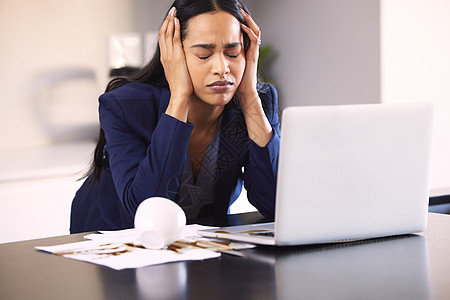 一位年轻女商务人士因咖啡洒在笔记本电脑上和桌子上的文件工作而心烦意乱的图片