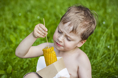金发可爱的男孩在夏天吃玉米 坐在绿草坪上 夏天 热天 零食图片