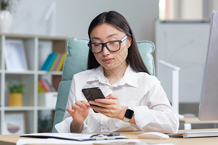 一位戴眼镜的亚洲女商务人士手里拿着电话 拨打一个信息 笑声人士互联网女性工作技术小样讨论职业微笑电脑图片