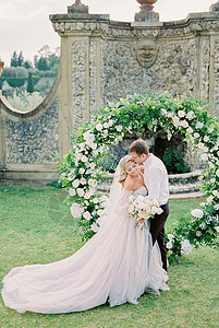Groom 在花园的婚礼拱门亲吻新娘图片