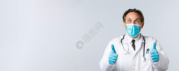 Covid19 预防病毒 医护人员和疫苗接种概念 戴着医用口罩和手套的兴奋而惊讶的快乐医生 兴奋地竖起大拇指 听到好消息 同意并图片