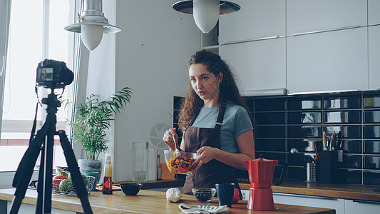 迷人的女孩在家里的厨房里用数码相机录制关于健康烹饪的视频食物 vlog Vlogging 和社交媒体概念图片