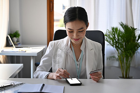 拥有信用卡 使用智能电话在线银行业务的漂亮女商务人士 (笑声)图片