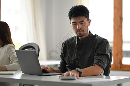 在办公室服务台使用笔记本电脑和使用计算器的英俊商务人士 从事笔记本电脑工作图片