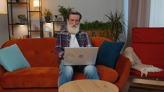 高级祖父男子自由职业者在笔记本电脑上工作 发送信息 在家网上购买胡子公寓休闲商业祖父母退休技术活动桌面房子图片