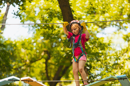 集中的女孩小心地克服了绳子公园中的障碍物冒险绳索娱乐乐趣活动闲暇行动挑战力量障碍图片
