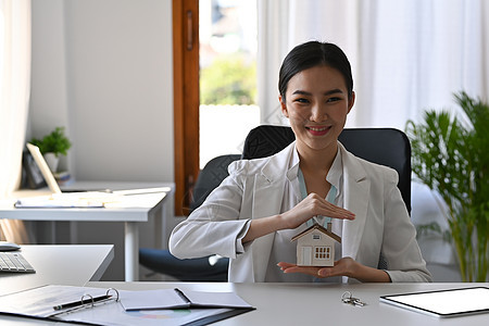 美丽的亚洲女性亲手保护房屋模型 保险或贷款房地产概念 (笑声)图片