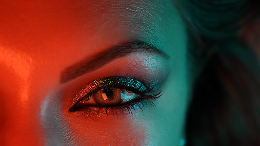 橙色蓝色霓虹灯下女人眼睛的特写镜头 美丽的妆容 闪闪发光的阴影的女性 美容 化妆品 夜总会生活方式概念图片