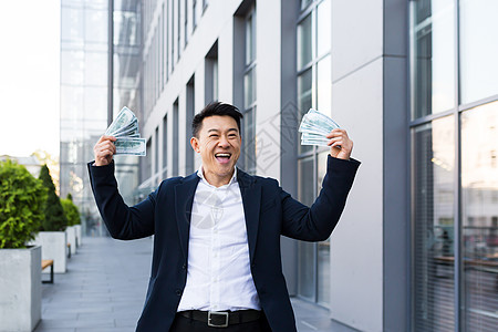 男性亚裔商务人士欢乐地拿着很多现金 赢得了大胜负和回报支付运气男人人士投资商务幸福情感活力惊喜图片