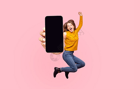 快乐的年轻女士在空中飞行和跳跃 显示巨大的移动空屏幕展示女孩飞跃手机空气粉红色享受广告喜悦蹦床图片