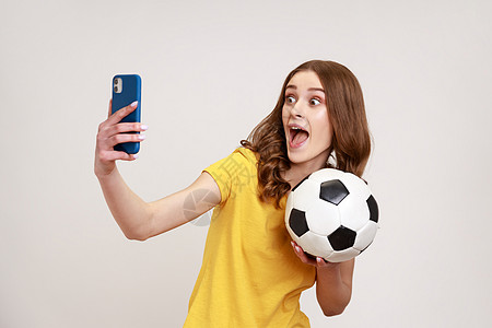 身穿黄色 vcasual T 恤 手持足球 直播足球比赛现场直播的年轻女博主喜出望外图片