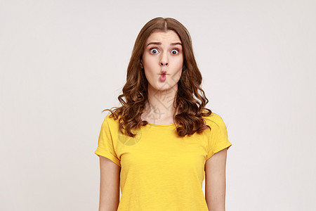 穿着黄T恤长着卷发的迷人有趣的少女肖像显示 鱼嘴唇尖锐 面对严酷的面孔 使幼稚可笑的滑稽讽刺图片
