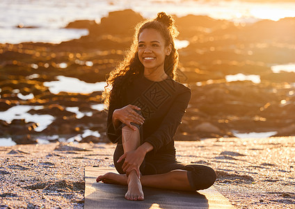 瑜伽是活在当下的练习 一位迷人的年轻女子在日落时分在海滩上的瑜伽课上坐在她的瑜伽垫上图片