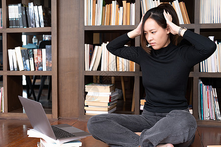 不快乐的年轻女学生感到疲倦准备考试 阅读书籍 网上冲浪信息 在抄写本上写笔记 在现代大学图书馆过度劳累图片