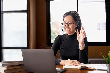 亚洲成年女性戴着耳机使用笔记本电脑 参加在线课程 虚拟课程 听力网络研讨会 观看培训 写笔记 进行视频通话 网上远程学习技术学校图片