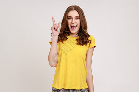 身穿黄色休闲 T 恤 举起手指 拥有天才创意的快乐灵感年轻女性肖像 看起来对突然的聪明想法感到惊讶图片