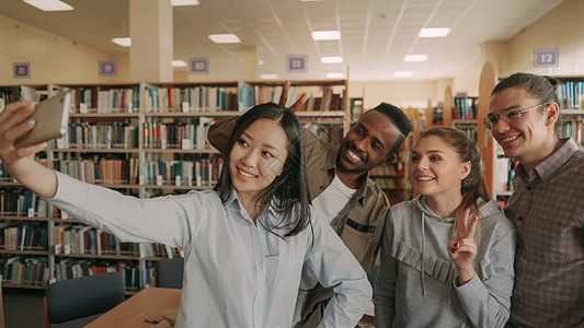 一群国际学生在大学图书馆的智能手机相机上开心地笑着自拍 快乐的朋友在一起进行预项目时休息女性乐趣照片成人团队社交鬼脸同学媒体微笑图片